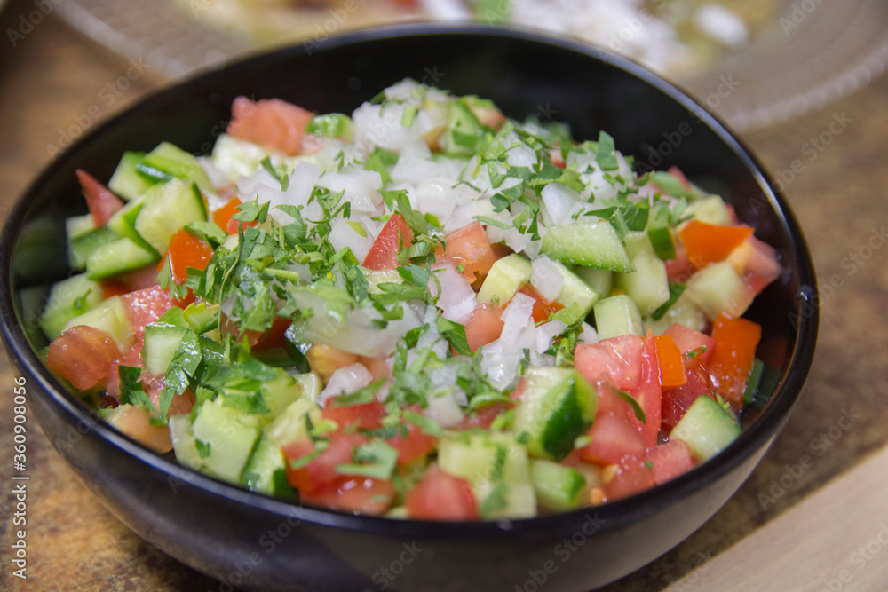 Fresh Israeli vegetables salad, containing cucumber, tomato white onion and parsley, served in a dark bowl Fresh Israeli vegetables salad, containing cucumber, tomato white onion and parsley, served in a dark bowl