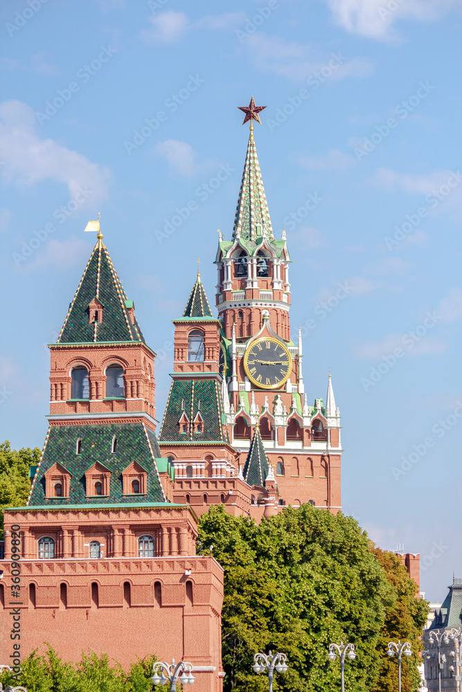 View of Spasskaya Tower of Moscow Kremlin above trees on a summer morning. Blue sky with few clouds in the background. Theme of travel in Russia.