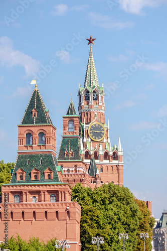 View of Spasskaya Tower of Moscow Kremlin above trees on a summer morning. Blue sky with few clouds in the background. Theme of travel in Russia.