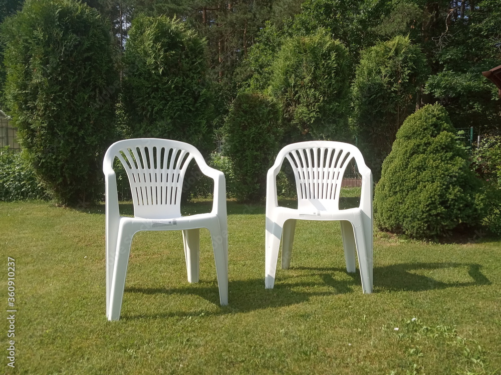 two white plastic chairs stand on the lawn, garden furniture
two white plastic chairs stand on the lawn, garden furniture