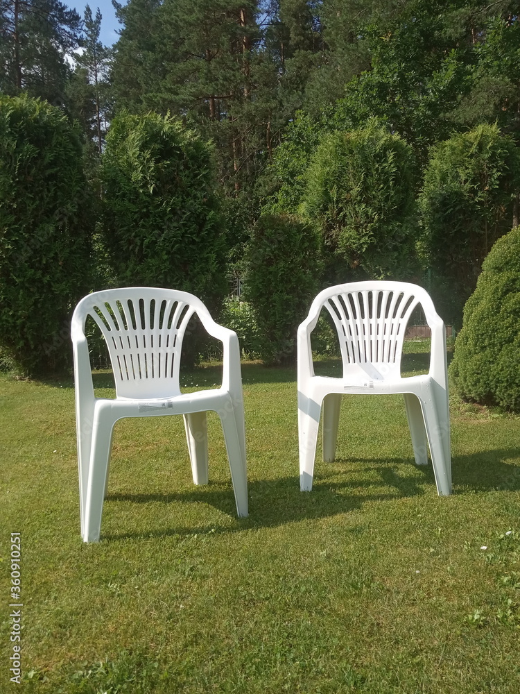 two white plastic chairs stand on the lawn, garden furniture
two white plastic chairs stand on the lawn, garden furniture