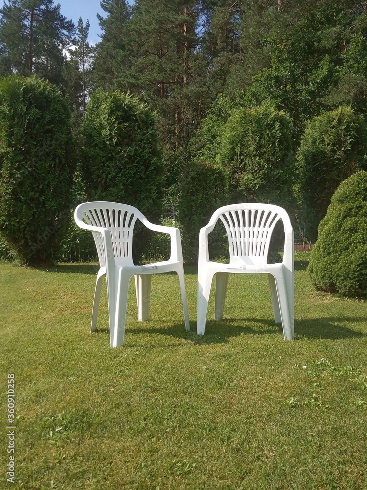two white plastic chairs stand on the lawn, garden furniture
two white plastic chairs stand on the lawn, garden furniture