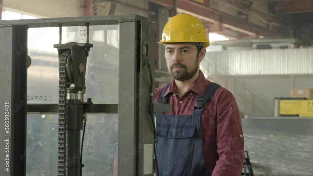 Portrait of man in hard hat and uniform inside factory workshop, driving loader Portrait of man in hard hat and uniform inside factory workshop, driving loader