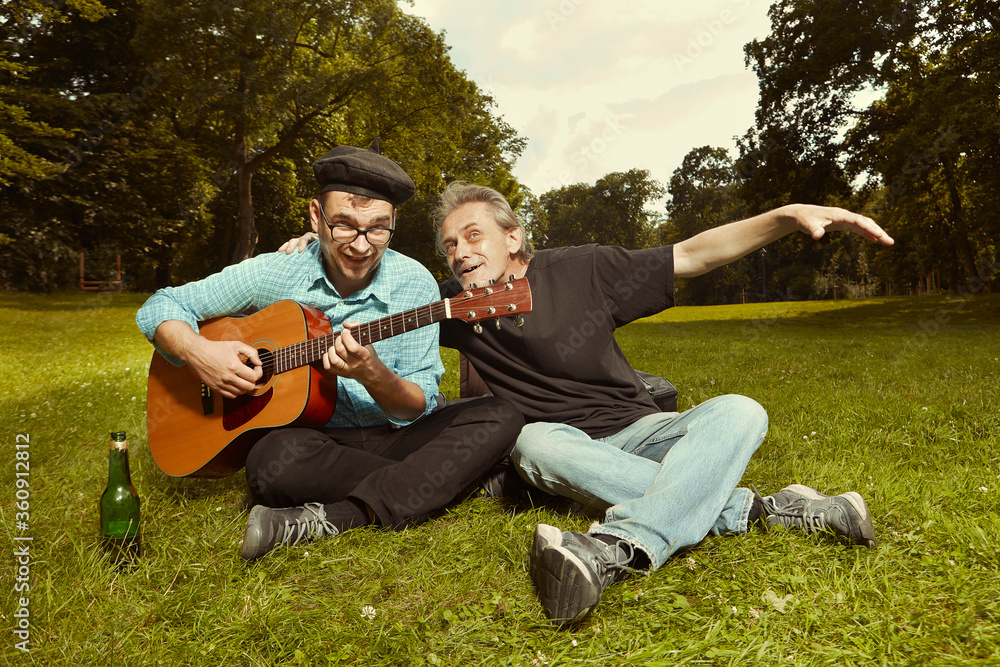 Two men on city park summer meadow enjoying day with guitar Two men on city park summer meadow enjoying day with guitar