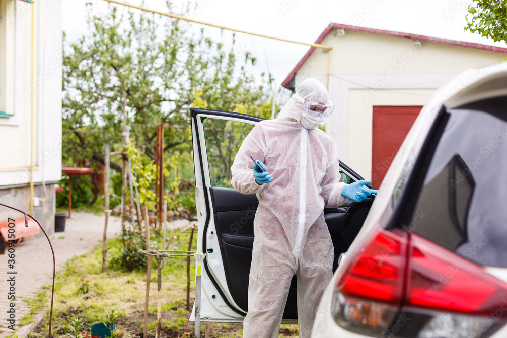 Man wearing a personal protective equipment suit, gloves, surgical mask and face shield, testing covid-19 coronavirus on another man sitting in a car.