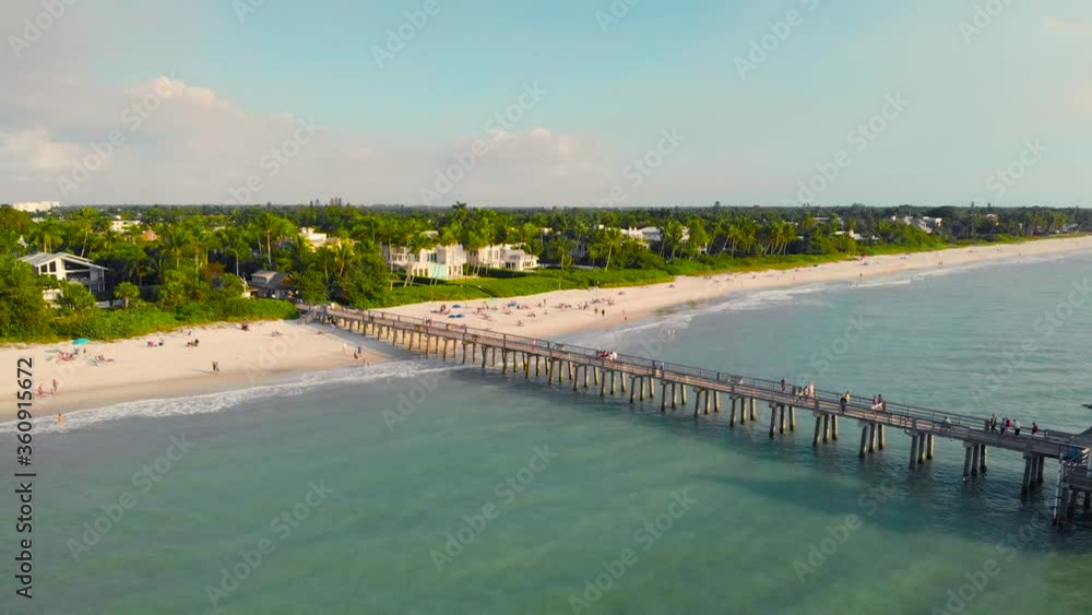 Sunset over the Gulf of Mexico, Drone flying above pier. Naples, Florida is a tourist town in the USA. People on Pier in a Calm Ocean. View from the ocean to the pier with tourists watching the sunset Sunset over the Gulf of Mexico, Drone flying above pier. Naples, Florida is a tourist town in the USA. People on Pier in a Calm Ocean. View from the ocean to the pier with tourists watching the sunset