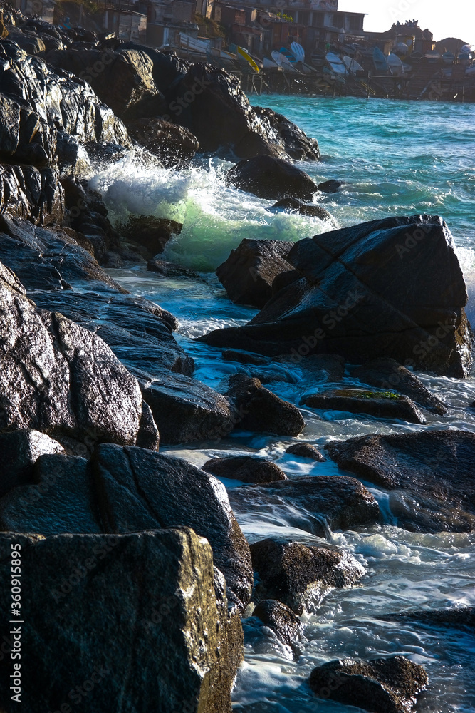 waves crashing on rocks with splashes in the background fishing village with small boats anchored with people silhouette on the rock waves crashing on rocks with splashes in the background fishing village with small boats anchored with people silhouette on the rock