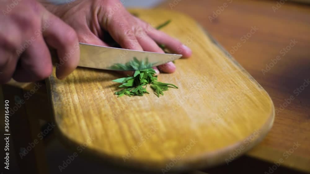 Cook cuts tarragon on a wooden board, with a kitchen knife Cook cuts tarragon on a wooden board, with a kitchen knife