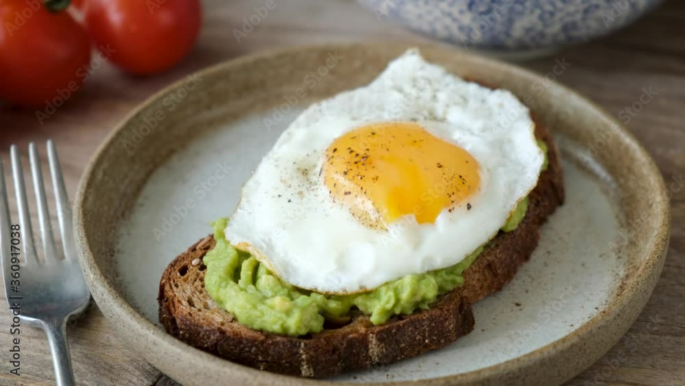 Rye bread toast with mashed avocado and sunny side up egg. Knife cutting egg yolk