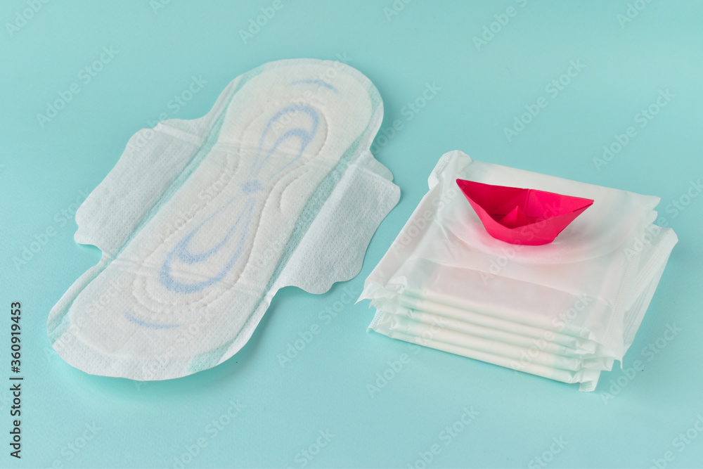 Sanitary napkin with a paper red boat on a turquoise background. The concept of critical days, menstruation. Gynecology. PMS Sanitary napkin with a paper red boat on a turquoise background. The concept of critical days, menstruation. Gynecology. PMS