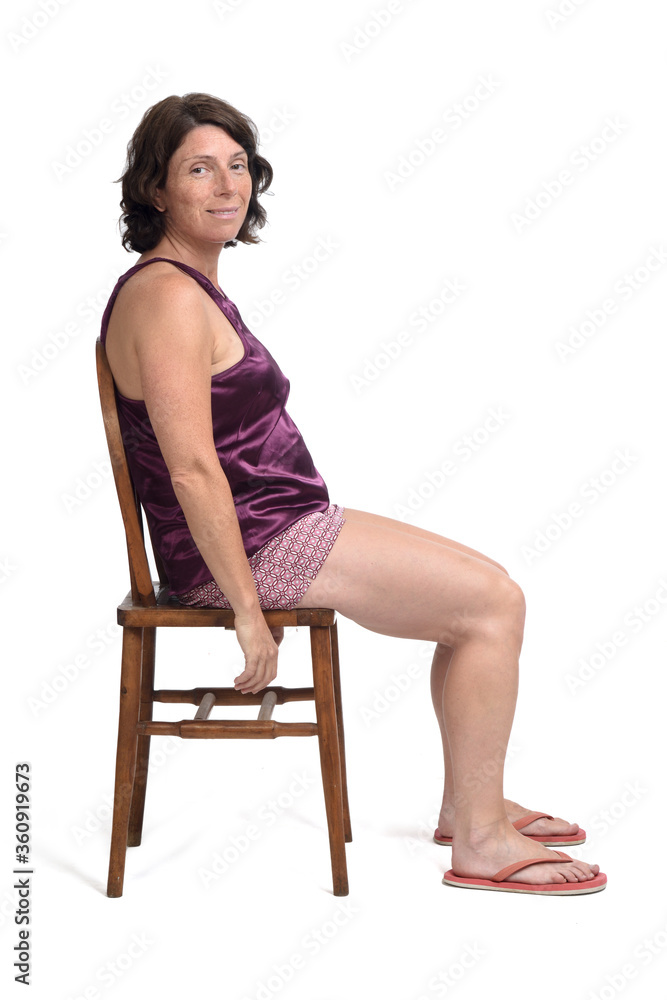 woman sitting on a chair dressed in a short summer pajamas on white background,side view and looking at camera