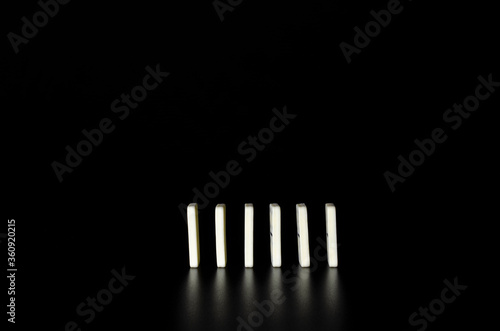 Six white domino blocks standing up in one straight line on black background