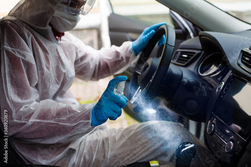 Cleansing car interior and spraying with disinfection liquid. Hands in rubber protective glove disinfecting vihicle inside for protection from virus disease