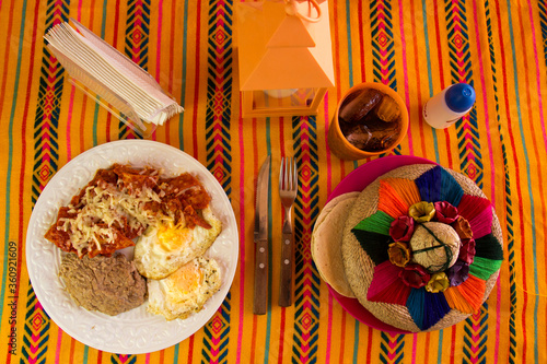 Huevos estrellados con chilaquiles y frijoles refritos puestos en una mesa de una restaurante con un ambiente mexicano