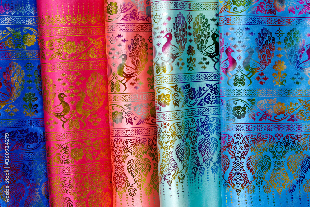 Lengths of colorful silk fabric with a peacock and floral motif for sale at an open-air market in Xishuangbanna, Yunnan Province, China Lengths of colorful silk fabric with a peacock and floral motif for sale at an open-air market in Xishuangbanna, Yunnan Province, China