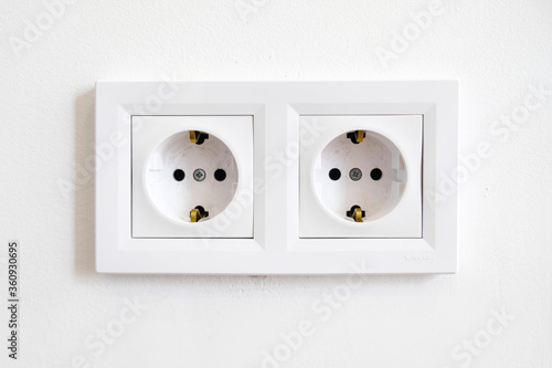 Pair of white European high voltage 220W sockets front on a white wall. Typical modern home interior. Essentials in redecorating and house remodeling. Electricity and power conservation in Europe. photo