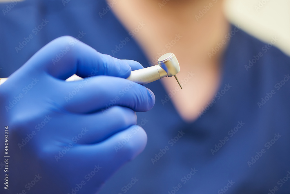 A close photo of a hand of a dentist who holds a dental diamond drill in the turbine stainless handpiece. A close photo of a hand of a dentist who holds a dental diamond drill in the turbine stainless handpiece.