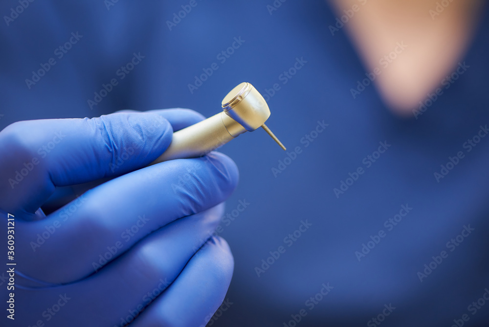 A close photo of a hand of a dentist who holds a dental diamond bur in the turbine stainless handpiece.