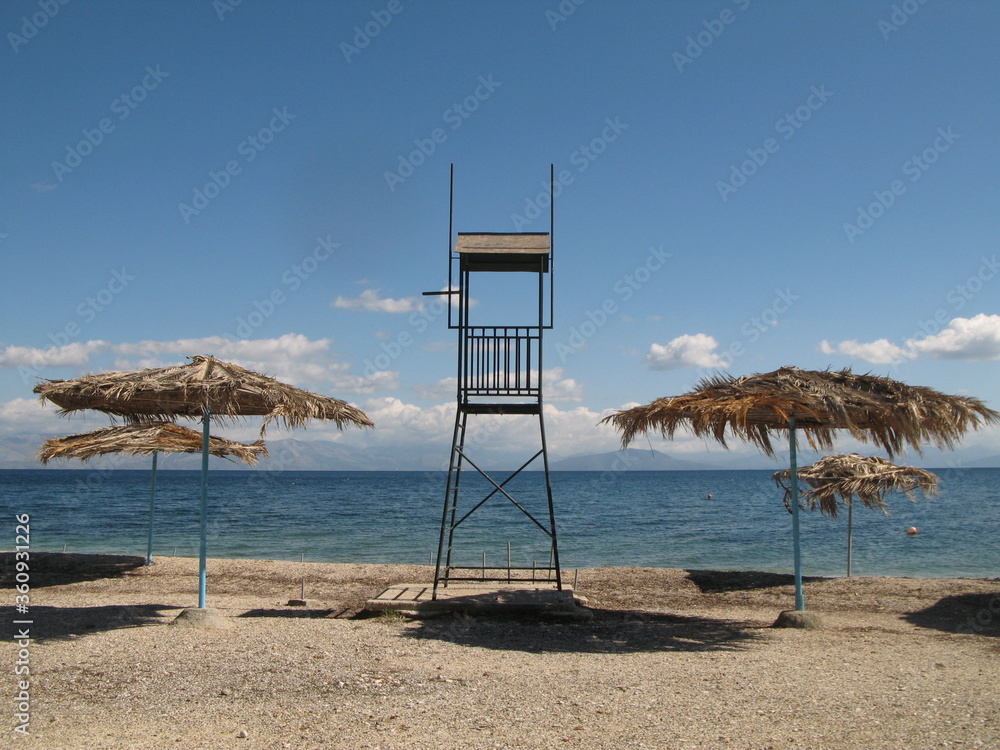 Beach near Perama, Corfu Island, Greece - wicker beach parasols and lifeguard tower Beach near Perama, Corfu Island, Greece - wicker beach parasols and lifeguard tower