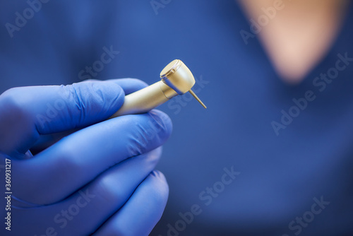 A close photo of a hand of a dentist who holds a dental diamond bur in the turbine stainless handpiece.