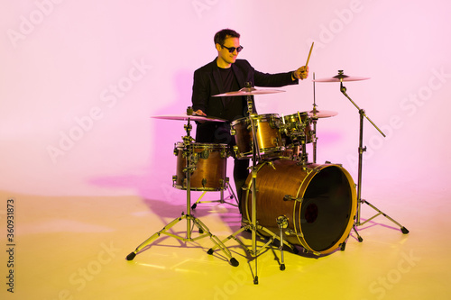 Caucasian male drummer improvising isolated on light studio background in neon light. Performing, looks inspired, energy. Concept of human emotions, facial expression, ad, music, art, festival. photo