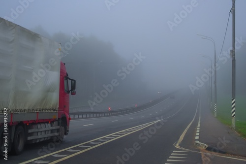 Early morning driving truck on highway in fog. Autumn, dry weather, foggy grey sky. One truck on the road. Lonely vehicle on the motorway.