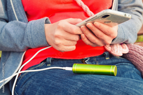 A girl uses a smartphone outdoors while charging from an external power bank