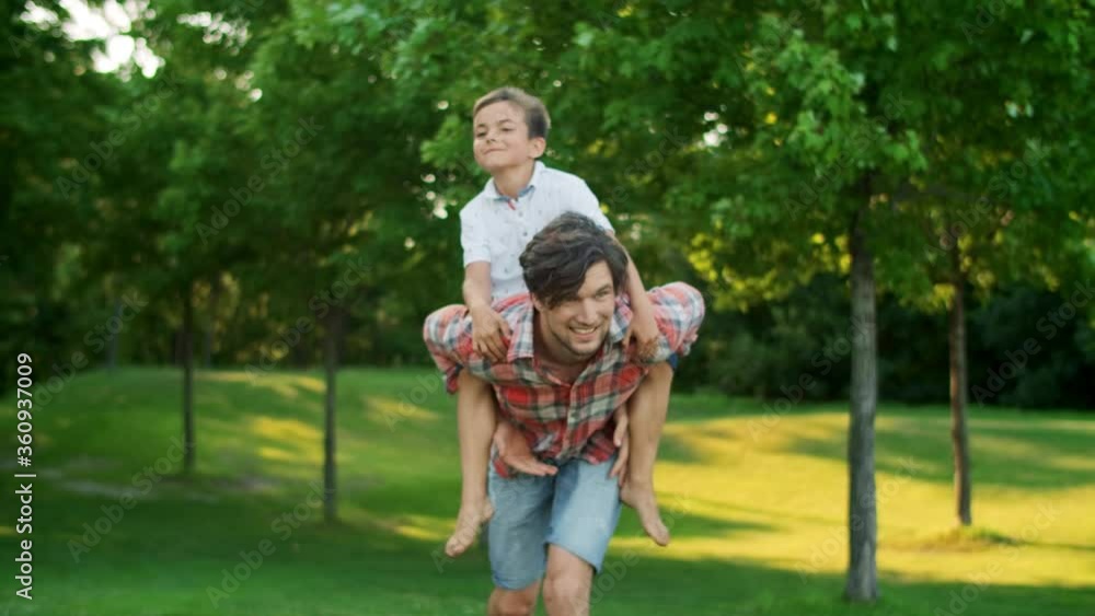 Boy jumping on man back in field. Portrait of happy father carrying son on back Boy jumping on man back in field. Portrait of happy father carrying son on back