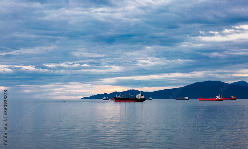 Ocean ships in Vancouver Harbor against the backdrop of a snow covered mountain ridge and cloudy sky Ocean ships in Vancouver Harbor against the backdrop of a snow covered mountain ridge and cloudy sky