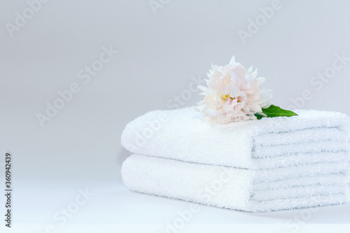 Two white neatly folded terry towels with a delicately pink peony flower on a light background.