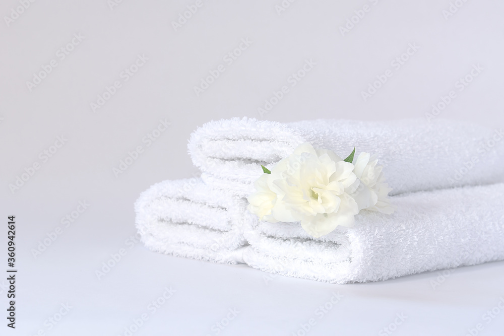 Three white neatly folded terry towels with a jasmine flower on a light background. Three white neatly folded terry towels with a jasmine flower on a light background.