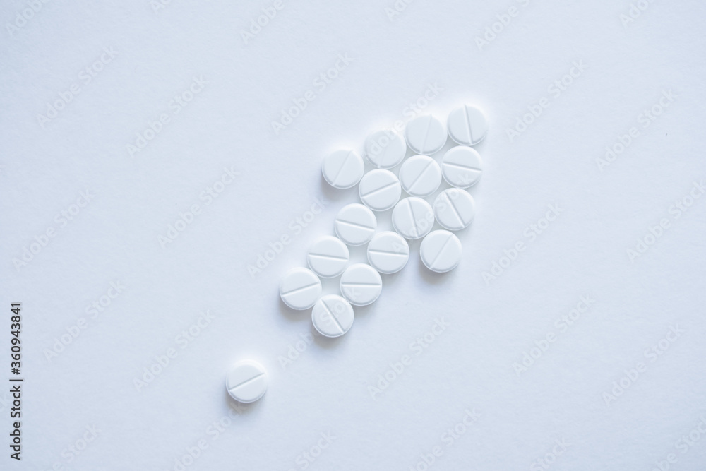 Pills laid out on a white background in the shape of an arrow shape pointing up. The concept of development, growth, increase in volume and business growth. For a pharmaceutical company. Top wiew.