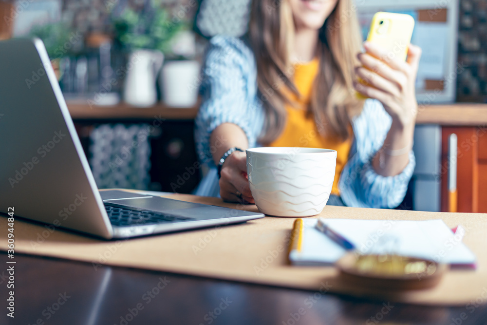 Business woman having a facetime video call. Happy and smiling girl working from home office kithcen and drinking coffee. Using computer and mobile phone. Distance learning online education and work Business woman having a facetime video call. Happy and smiling girl working from home office kithcen and drinking coffee. Using computer and mobile phone. Distance learning online education and work