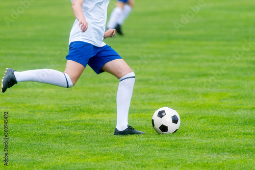 Young woman soccer player kicks ball on football field. Team sport concept..