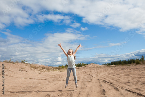 Happy child girl jumping against sky clouds outdoors