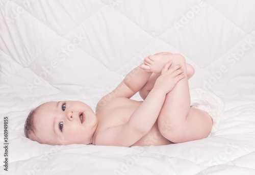 Happy sweet little baby boy playing with his feet, white background