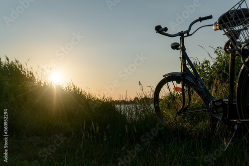 Vintage classic bicycle with nature green backgrounds with water lake river sunset on grass field  © Chan2545