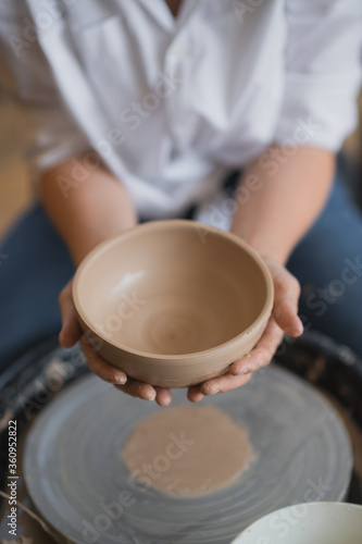 The female potter finished making a clay vase remove it from the potter's wheel. Creating vase of white clay. Making ceramic products from white clay, closeup