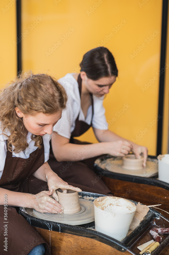 Two women make pottery on a pottery wheels, shaping clay by their hands, close up. Pottery craft workshop at art studio. Two women make pottery on a pottery wheels, shaping clay by their hands, close up. Pottery craft workshop at art studio.