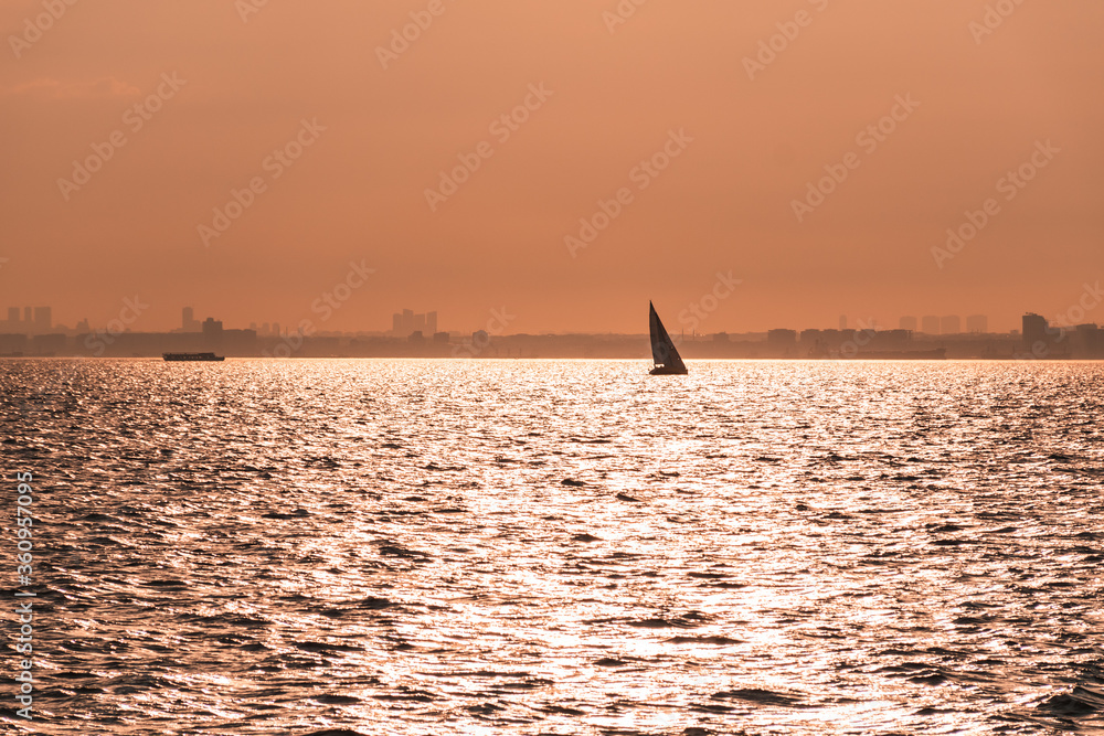 a sailboat meets the sunset in the last bright sun lights falling on the sea.