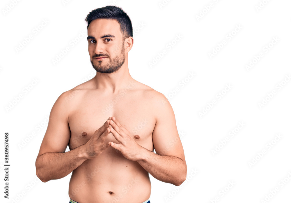 Young handsome man wearing swimwear hands together and fingers crossed smiling relaxed and cheerful. success and optimistic Young handsome man wearing swimwear hands together and fingers crossed smiling relaxed and cheerful. success and optimistic