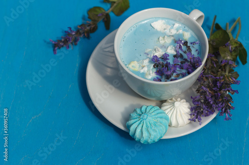 Blue moon milk decorated with blue flowers and meringue crumbs on a bright blue background