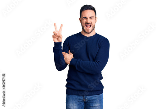 Young handsome man wearing casual clothes smiling with happy face winking at the camera doing victory sign. number two.