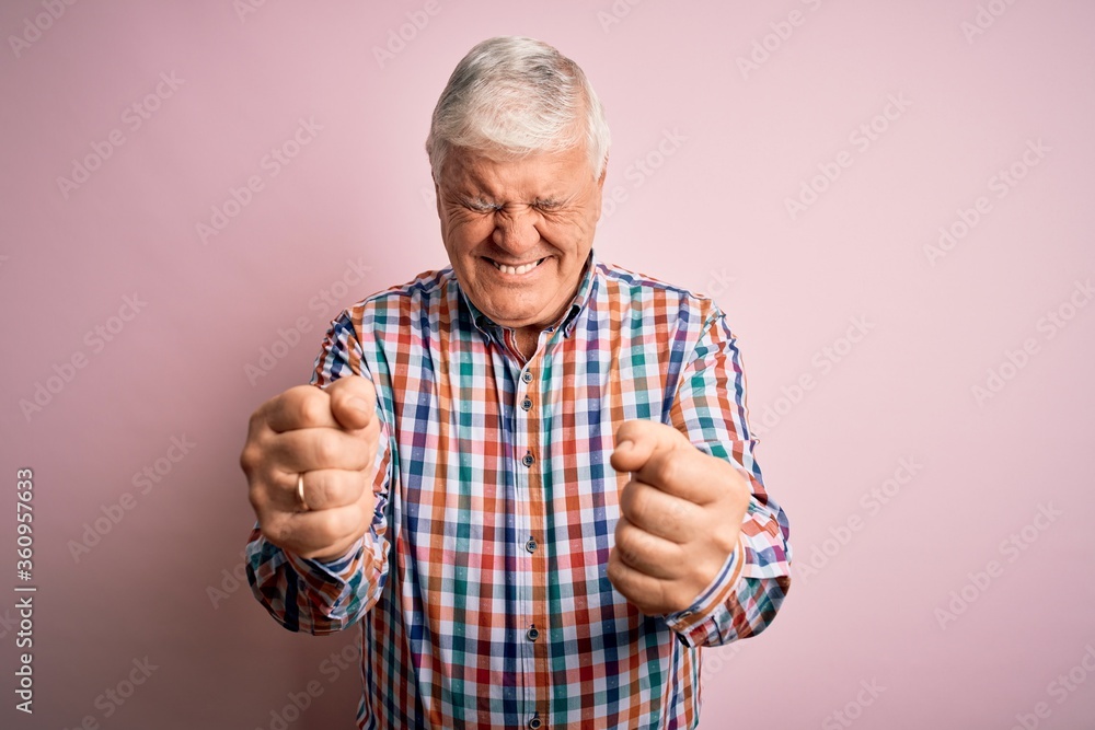 Naklejka premium Senior handsome hoary man wearing casual colorful shirt over isolated pink background excited for success with arms raised and eyes closed celebrating victory smiling. Winner concept.