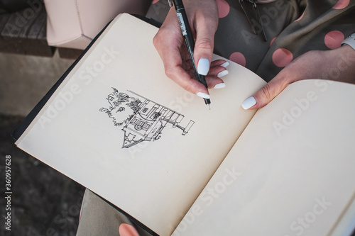 Sketchbook with a drawing of a house close-up. Girl draws in the fresh air.