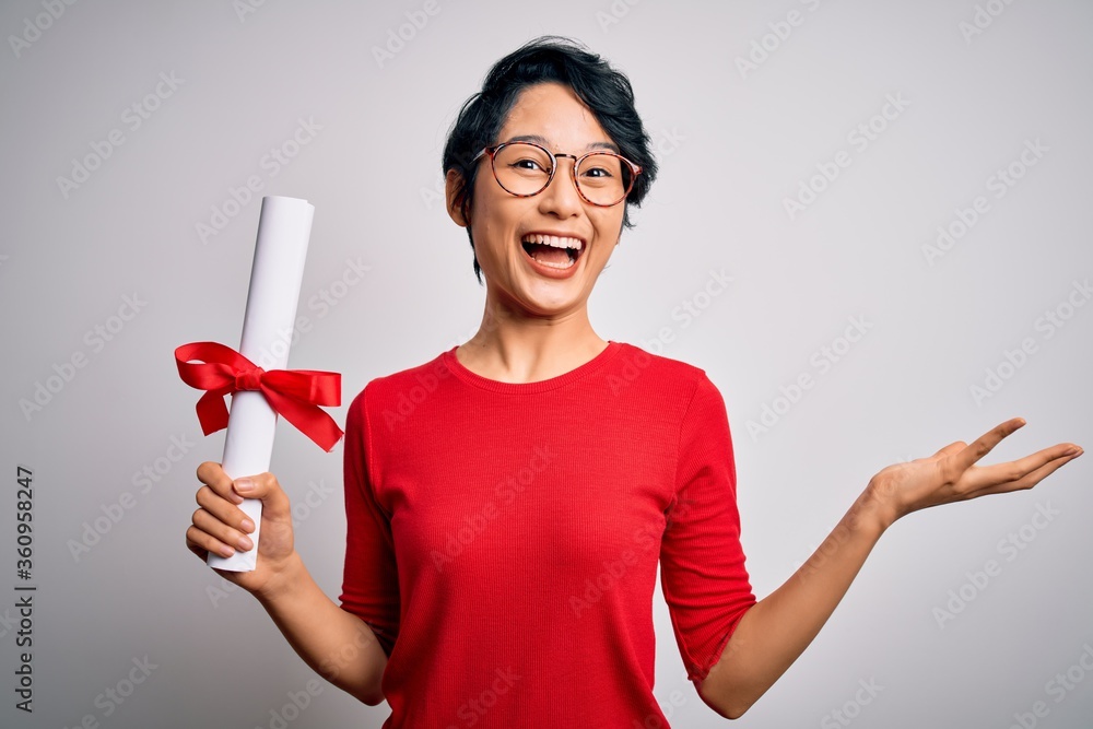 Beautiful chinese student woman wearing glasses holding university graduated diploma degree very happy and excited, winner expression celebrating victory screaming with big smile and raised hands Beautiful chinese student woman wearing glasses holding university graduated diploma degree very happy and excited, winner expression celebrating victory screaming with big smile and raised hands