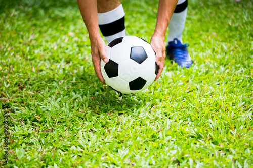Selective focus to soccer ball with blurry hands of players are putting it on green grass. © Koonsiri