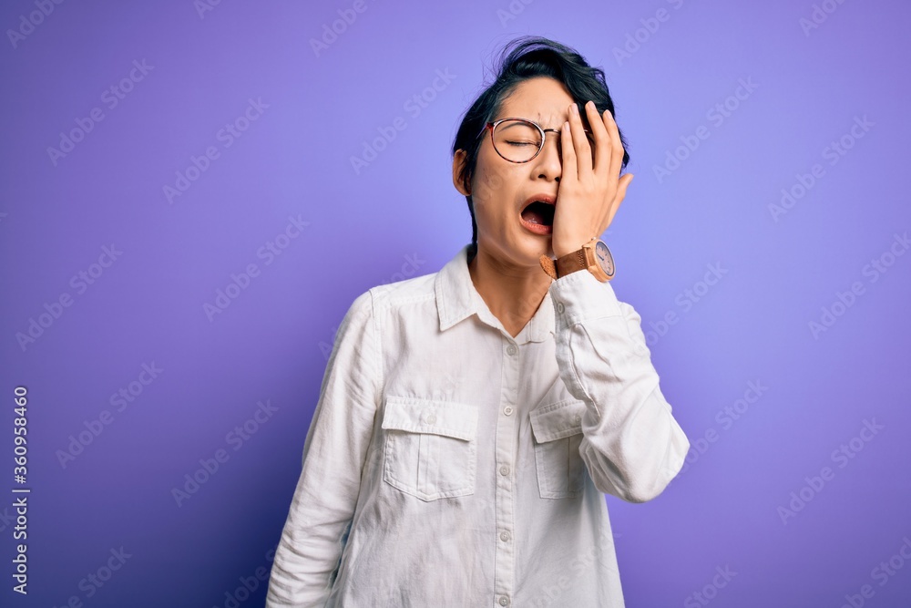 Young beautiful asian girl wearing casual shirt and glasses standing over purple background Yawning tired covering half face, eye and mouth with hand. Face hurts in pain. Young beautiful asian girl wearing casual shirt and glasses standing over purple background Yawning tired covering half face, eye and mouth with hand. Face hurts in pain.