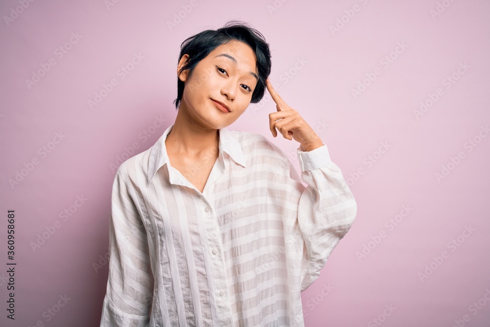 Young beautiful asian girl wearing casual shirt standing over isolated pink background Smiling pointing to head with one finger, great idea or thought, good memory