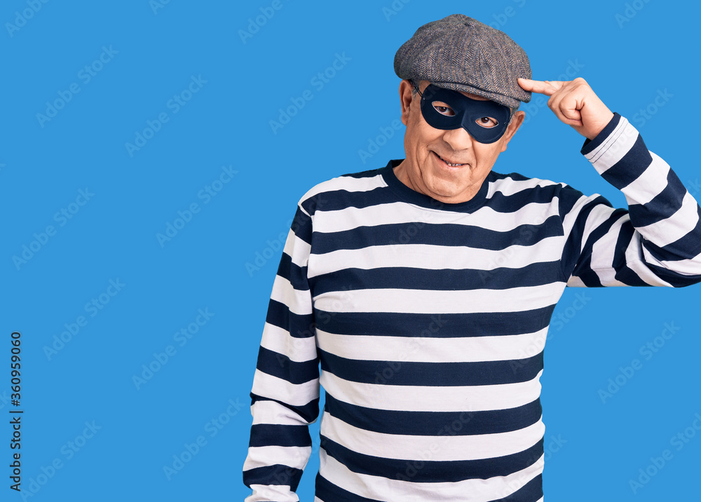 Senior handsome man wearing burglar mask and t-shirt smiling pointing to head with one finger, great idea or thought, good memory Senior handsome man wearing burglar mask and t-shirt smiling pointing to head with one finger, great idea or thought, good memory